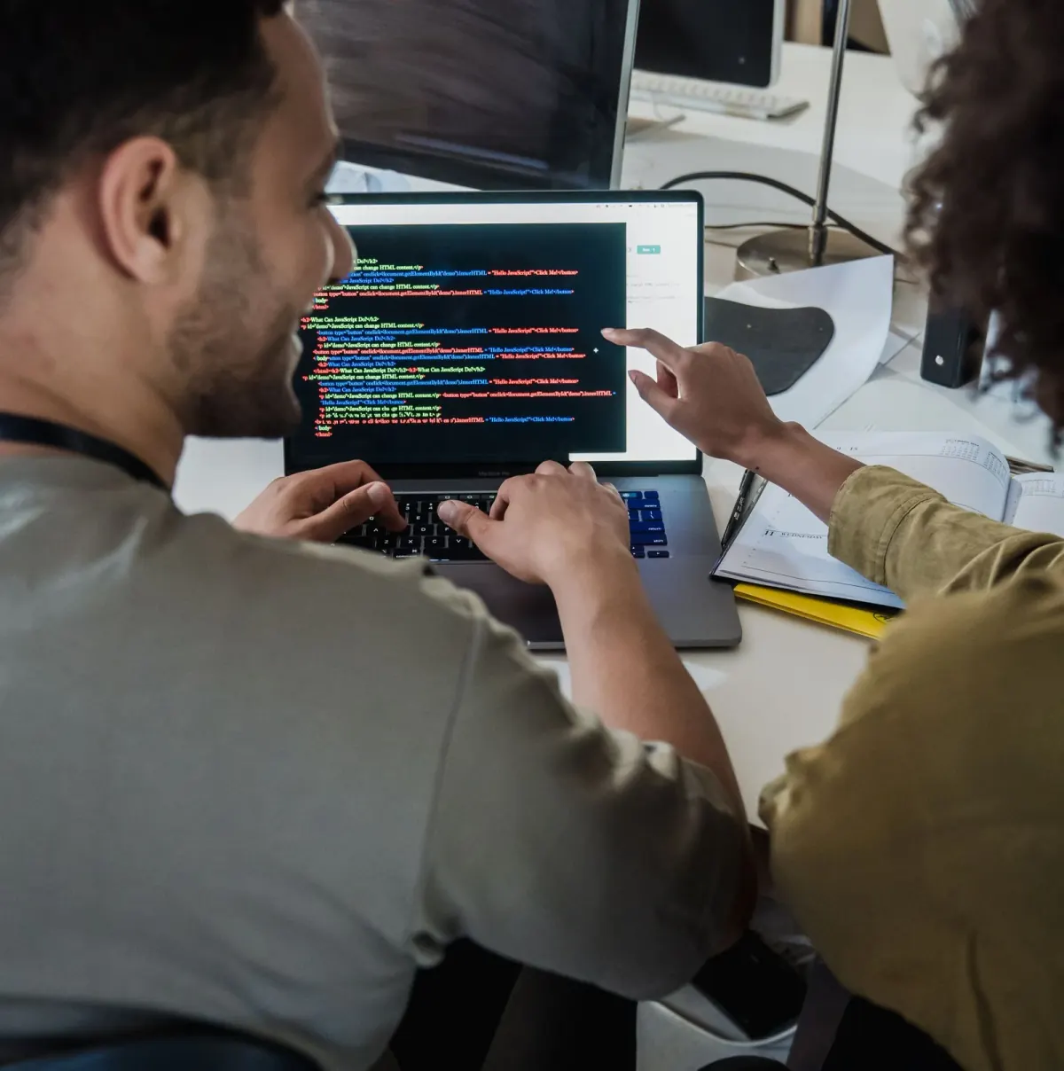 Two developers reviewing code together on a laptop, one pointing at the screen